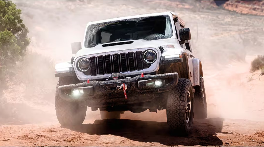 A Bright White Clear-Coat 2026 Jeep Wrangler Rubicon kicking up a dramatic cloud of dust as it accelerates down a rugged off-road trail near Morristown NJ, showcasing its signature black seven-slot grille, red front tow hooks, and integrated winch. 