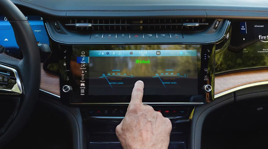 Driver hand adjusting McIntosh audio settings with illuminated VU meters on the 12.3-inch Uconnect 5 center screen and passenger interactive display inside a 2026 Jeep Grand Cherokee at Salerno Duane CJDR near Summit, NJ in Union County
