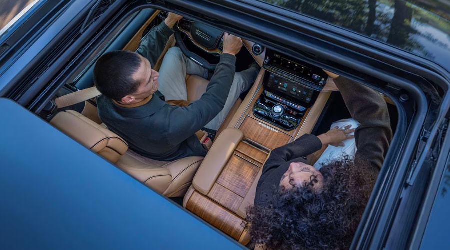 An overhead view looking through the panoramic sunroof of a 2026 Jeep Grand Wagoneer, highlighting the premium wood trim and tan leather front cabin for commuters navigating Route 18 in East Brunswick, NJ.