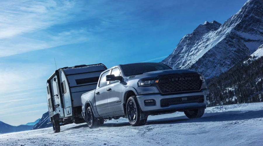 Silver 2027 Ram 1500 towing a heavy travel trailer through snowy road conditions, demonstrating 11,580-lb towing capacity and Hurricane twin-turbo engine power at Salerno Duane Chrysler Jeep Dodge Ram in Summit, NJ.