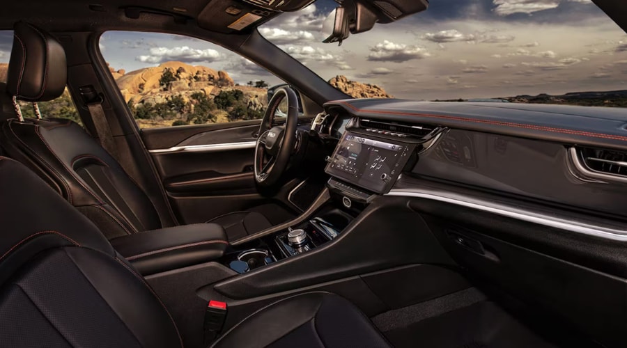 Passenger-side view of a 2026 Jeep Grand Cherokee luxury interior featuring dark leather seats with contrast red stitching, central Uconnect 5 screen, and sleek passenger dashboard display at Salerno Duane CJDR near Summit, NJ in Union County.