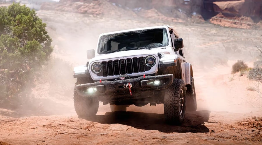 White 2026 Jeep Wrangler Rubicon navigating a dusty off-road trail with active front LED headlights, integrated Warn winch, and steel bumper, demonstrating Off-Road Pages capability for Summit and Morristown NJ drivers.