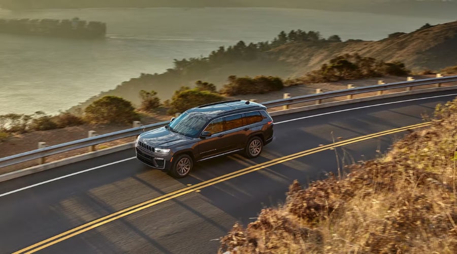 Dark gray 2026 Jeep Grand Cherokee cruising along a winding highway curve with Quadra-Lift air suspension active, available at Salerno Duane CJDR near Summit and Morristown, NJ in Union County.