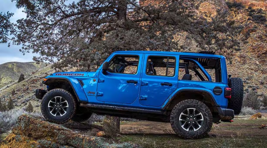 A Hydro Blue Pearl-Coat 2026 Jeep Wrangler Rubicon 4-door crawling over massive granite rock formations on a rugged off-road trail near Summit NJ, demonstrating its high ground clearance and live-axle suspension articulation