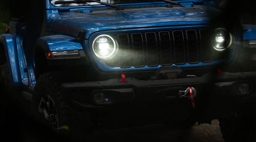 Hydro Blue 2026 Jeep Wrangler Rubicon front fascia with glowing circular LED headlights cutting through mist, showcasing the integrated front trail camera location and bumper radar sensors for Morristown and Union County drivers.