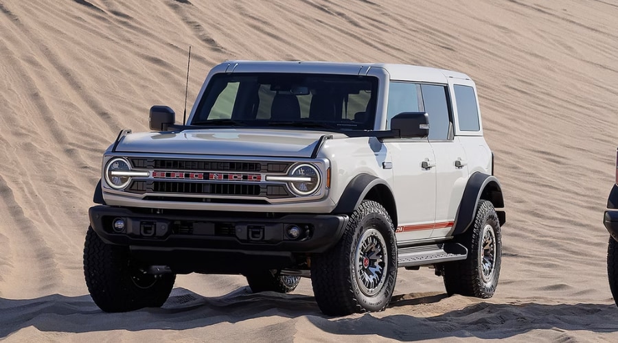 Front and rear view of two heritage-style 2026 Ford Bronco SUVs in white and red parked side-by-side on sand dunes, highlighting retro design options for Summit, NJ drivers.