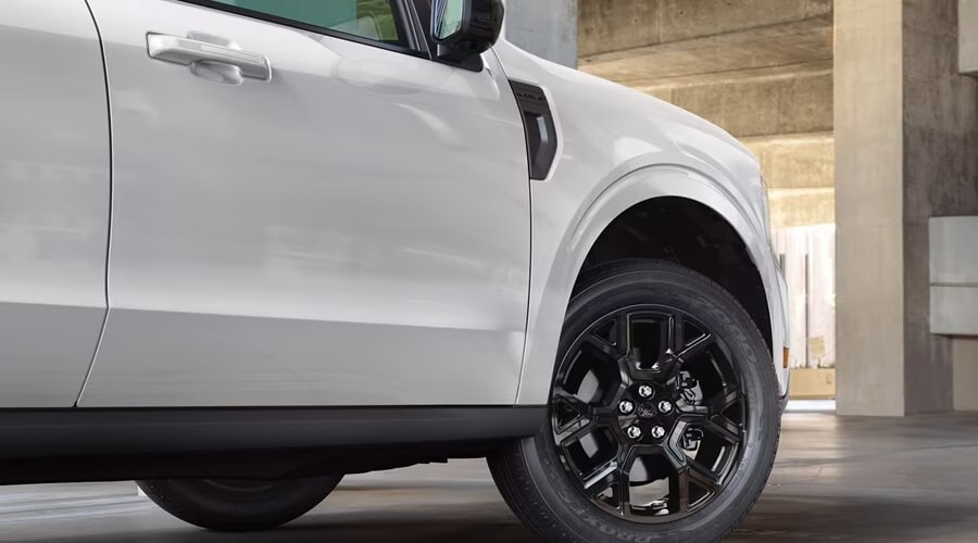 Side profile view of a white 2026 Ford Maverick Lobo street performance truck featuring gloss black alloy wheels, parked in a parking structure in Summit, NJ.
