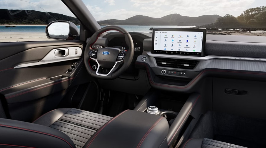 Interior cabin view of the 2026 Ford Explorer showing the 13.2-inch digital touchscreen, sport seats with red accent stitching, and modern driver-centric dashboard.