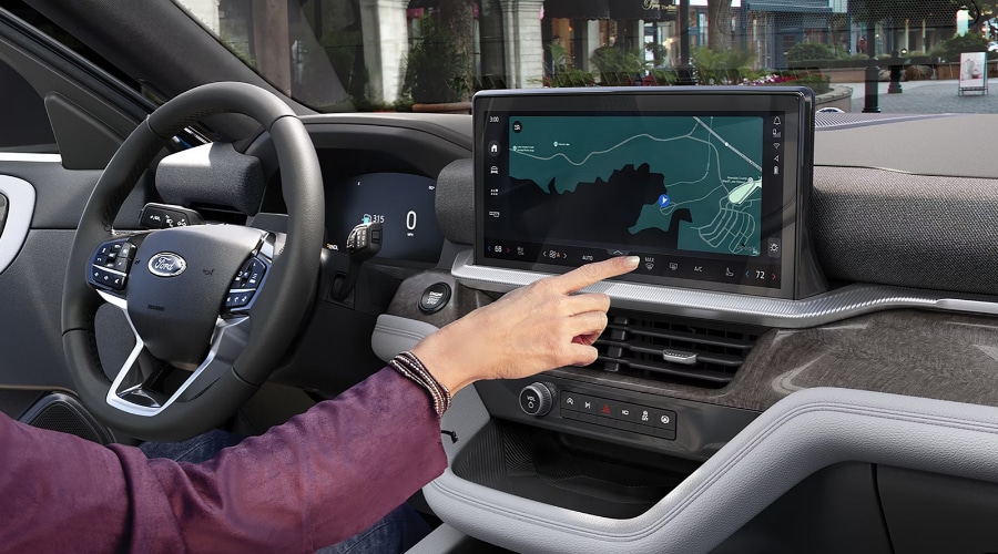 Driver tapping the 13.2-inch touchscreen display showing Google Maps navigation inside the updated 2027 Ford Explorer interior, featuring a digital instrument cluster and leather-wrapped steering wheel at Salerno Duane Ford near Summit, NJ. 