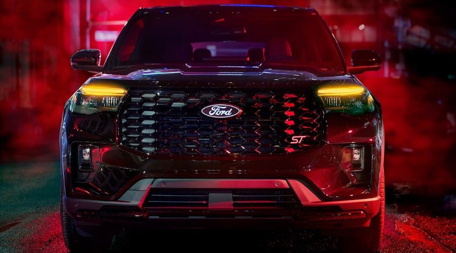 Front-facing view of a 2026 Ford Explorer ST with illuminated amber LED headlights and dark honeycomb grille parked on wet pavement at night, showcasing low-visibility safety tech and all-weather control for I-78 rainstorm commutes in Summit, NJ.