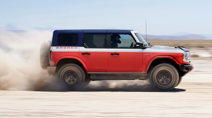 Side profile of a tri-color red, white, and blue 2026 Ford Bronco driving at high speed and kicking up a trail of dust, highlighting off-road performance for drivers near Summit, NJ.