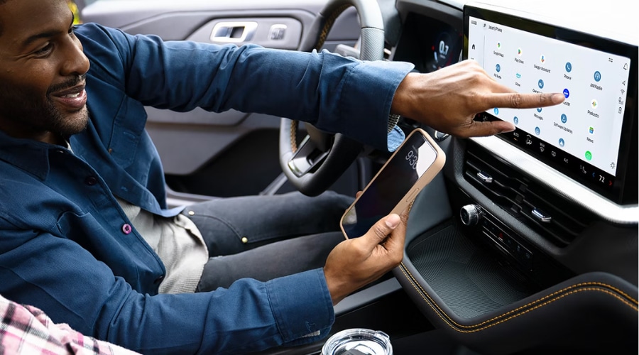 Driver pointing to the 13.2-inch Ford Digital Experience touchscreen inside a 2026 Ford Explorer to access native Google Maps navigation while holding a smartphone, demonstrating built-in 5G connectivity for suburban family commutes in Summit and Union County, NJ.