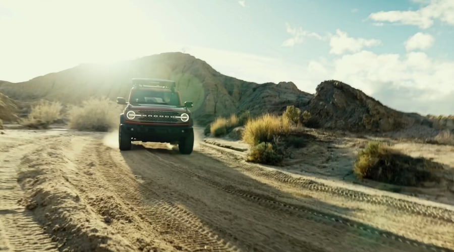 A rugged red 2026 Ford Bronco full-size 4x4 SUV navigating a dusty off-road dirt trail through a hilly landscape, highlighting its heavy-duty body-on-frame capability and advanced 4x4 performance for North Jersey weekend trail adventurers.