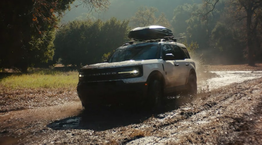 A white 2026 Ford Bronco Sport driving through a muddy, wet path surrounded by trees, demonstrating confident 4x4 traction and stability for autumn rainstorms across Summit, NJ, and Union County.