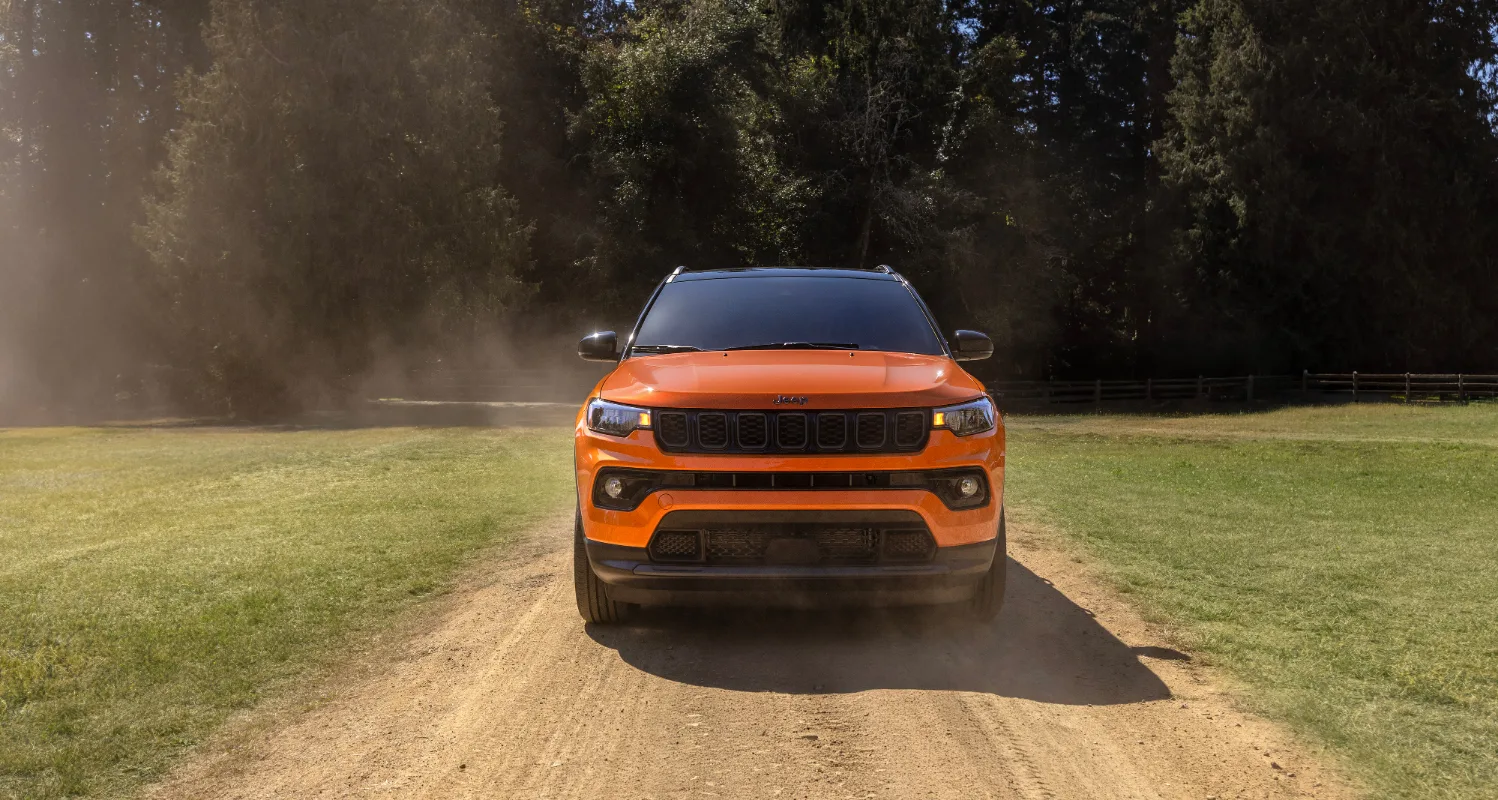 Front view of Orange Jeep Compass parked in front of trees