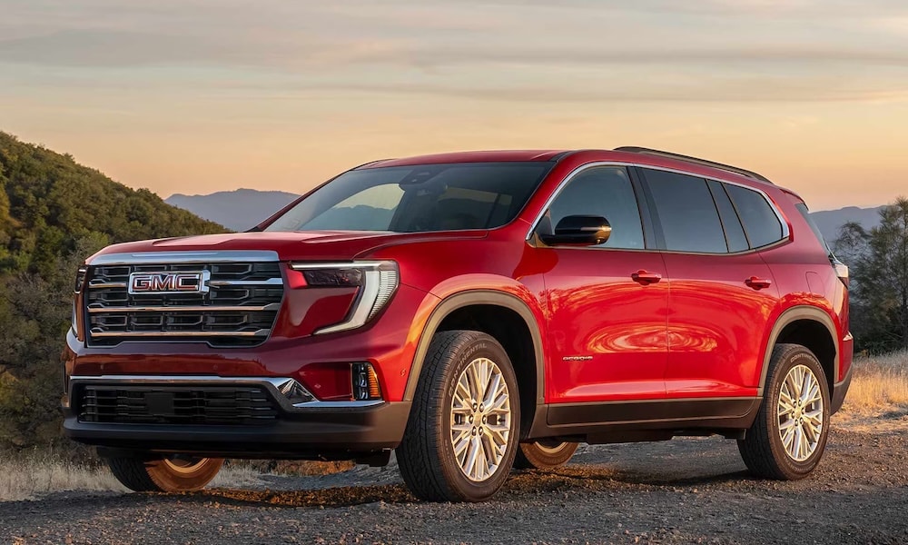A red 2026 GMC Acadia SUV driving down a dusty dirt road