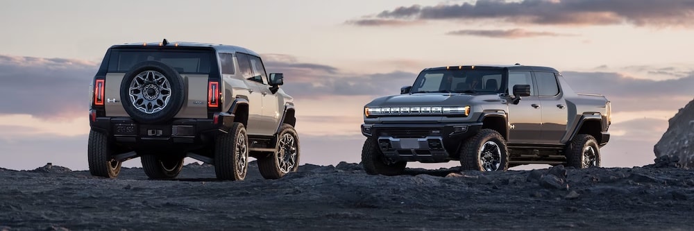 Two 2026 GMC Hummers parked on a rocky ledge at sunset