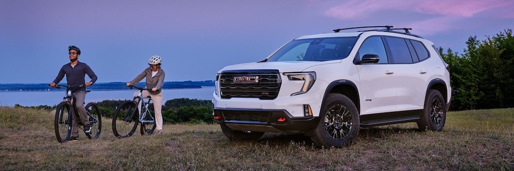 Two cyclists beside a white GMC SUV at sunset
