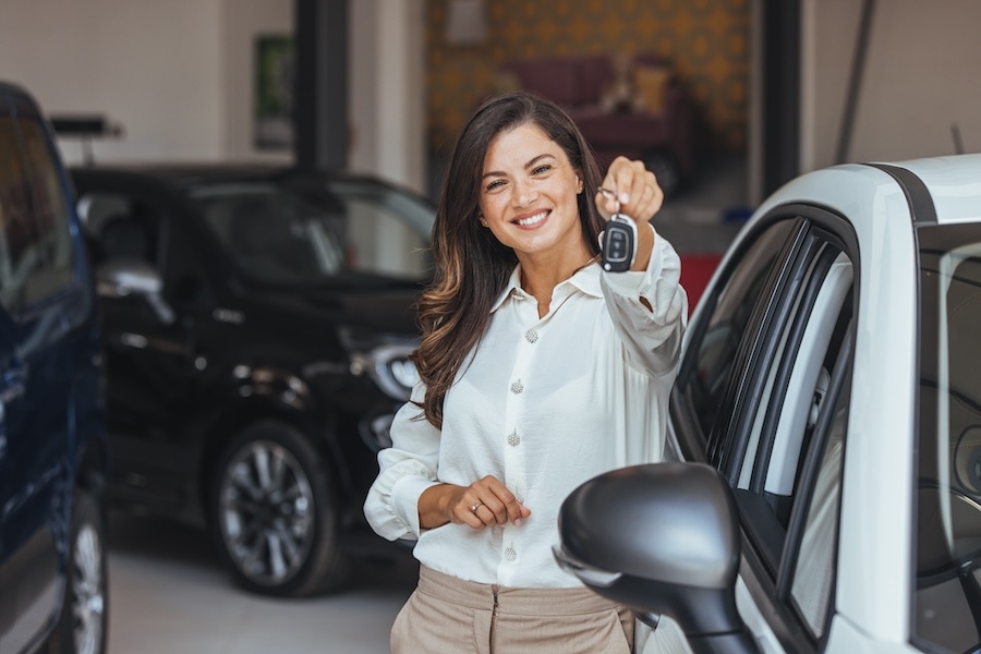 A woman holds out a car key inside a car dealership
