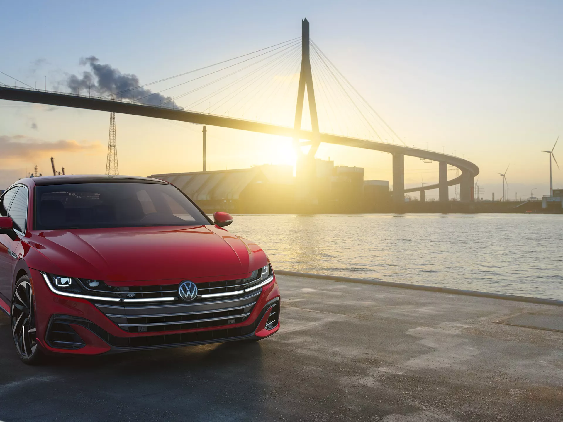 Arteon shown in Kings Red Metallic parked on waterfront with bridge in background.