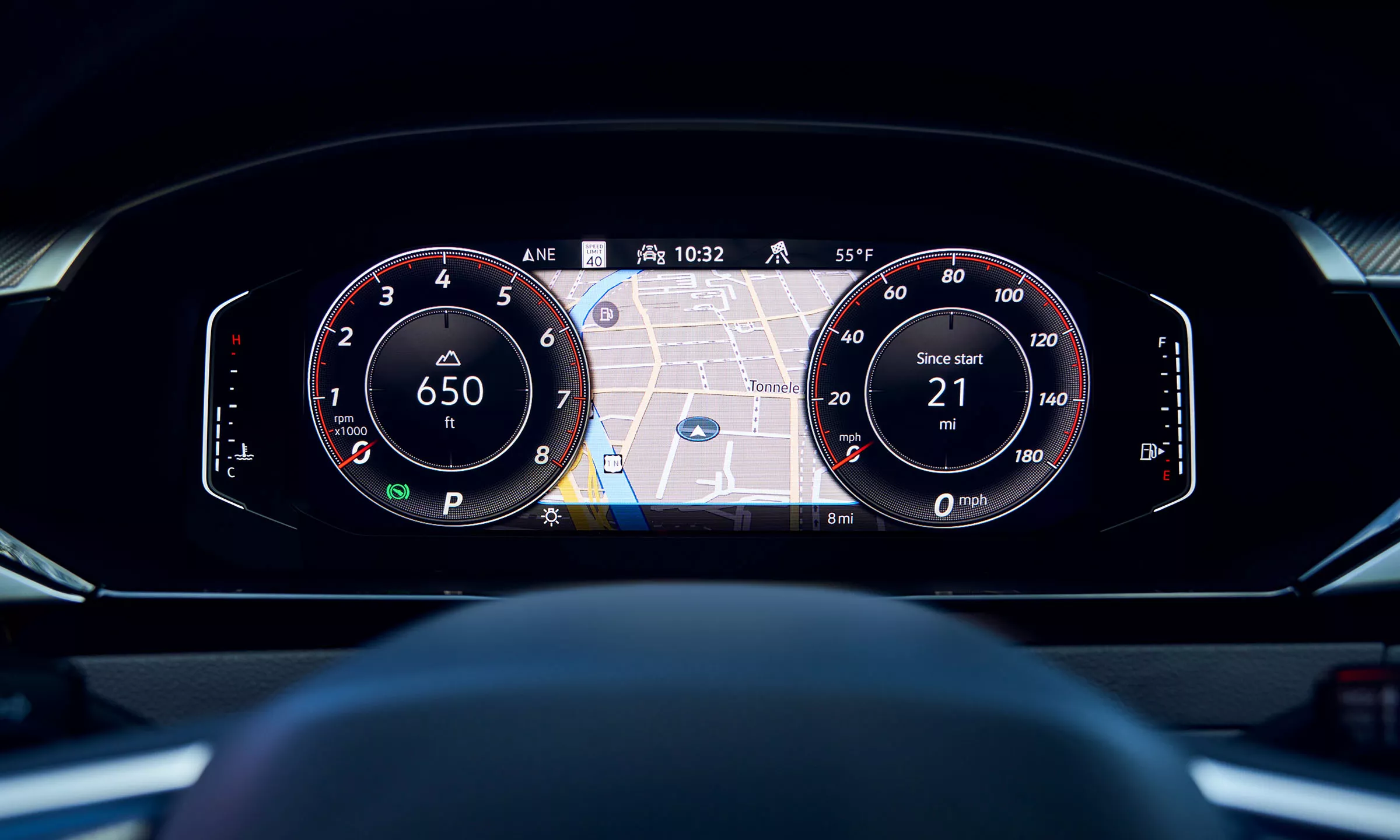 Close up on the VW Digital Cockpit Pro display as seen through the steering wheel, showing driving data, including elevation, distance travelled, navigation map with route cursor, rpm and mph, and temperature and gas gauges. 