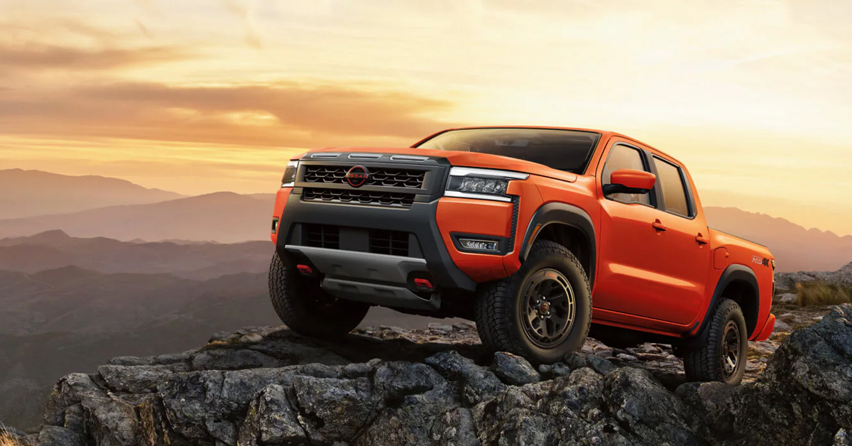 2026 Nissan Frontier navigating over a rocky outcrop, highlighted by an orange sky at sunset