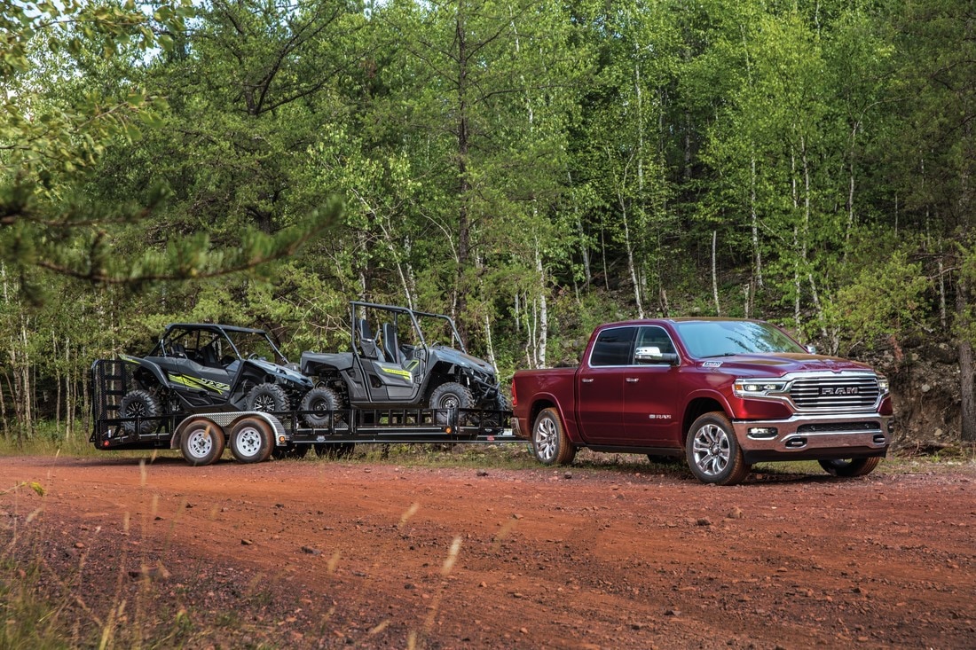 Ram 1500 parked on dirt road in woods with off-road vehicles hitched on trailer