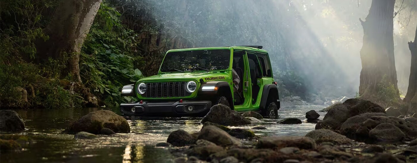 Green 2026 Jeep Wrangler Rubicon driving to a Jeep Dealer