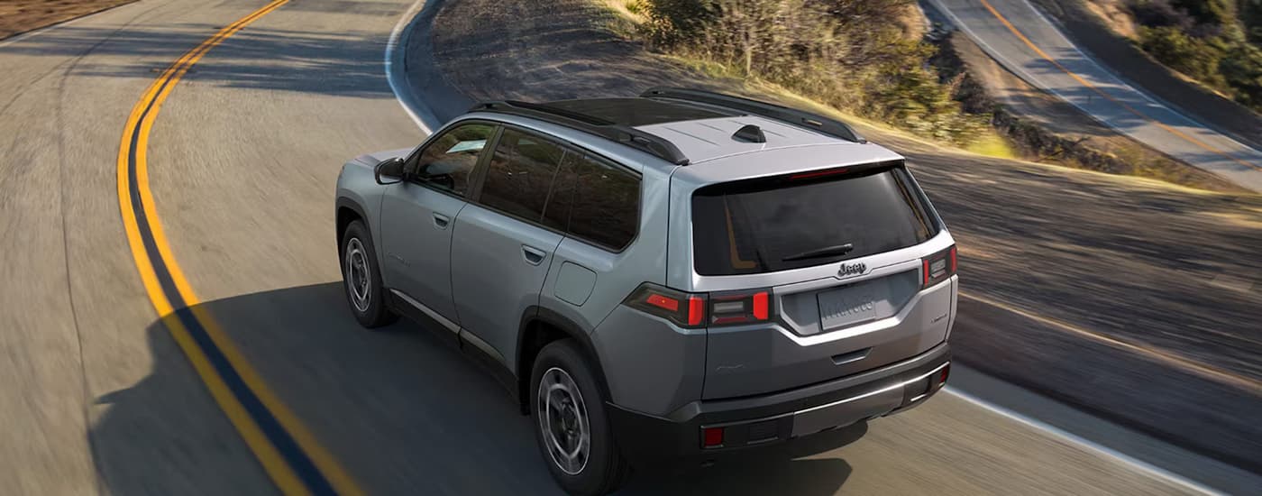 Rear of a silver 2027 Jeep Cherokee driving around a bend