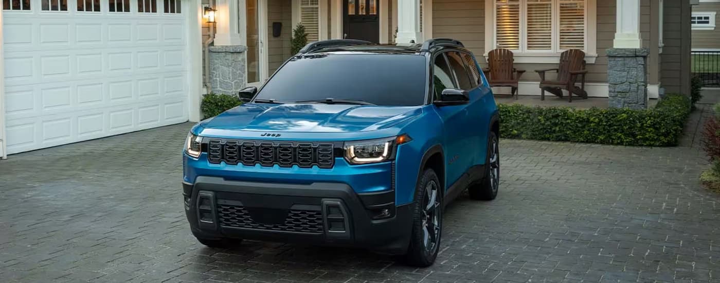 Blue 2027 Jeep Cherokee parked on a driveway in front of a house