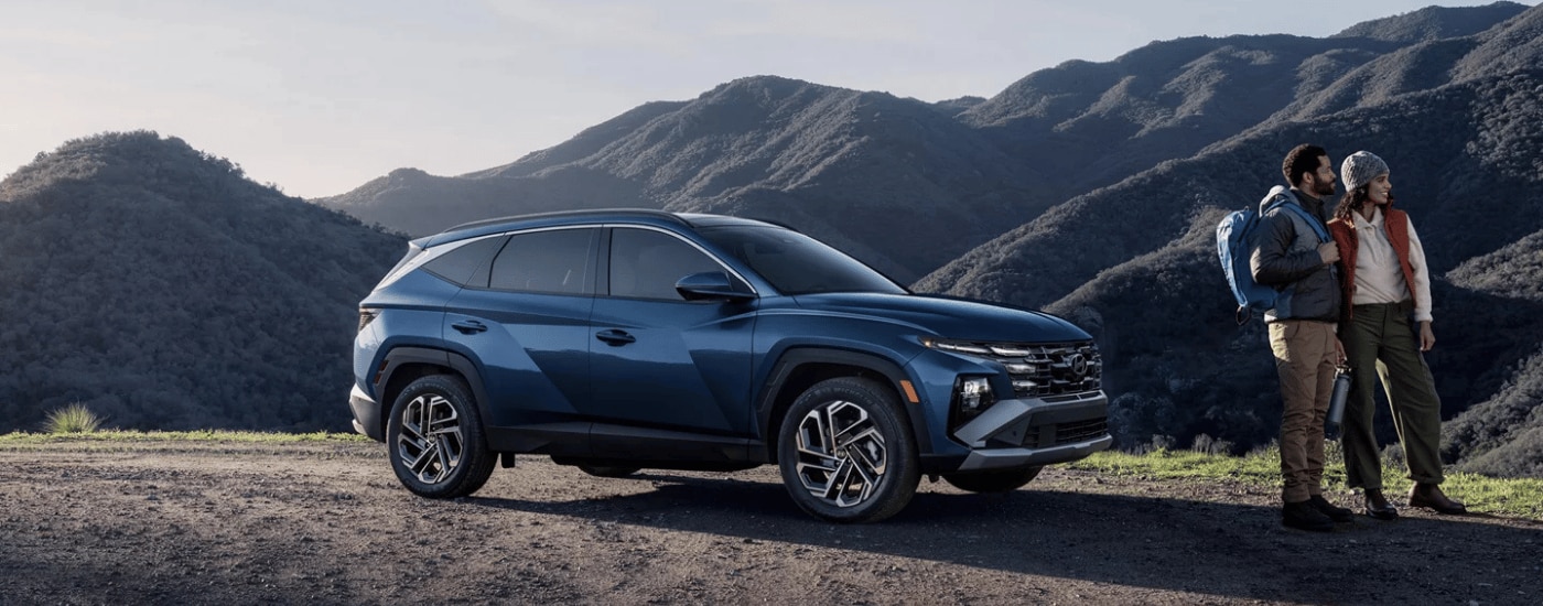 A couple standing in front of their blue 2026 Hyundai Tucson parked off-road
