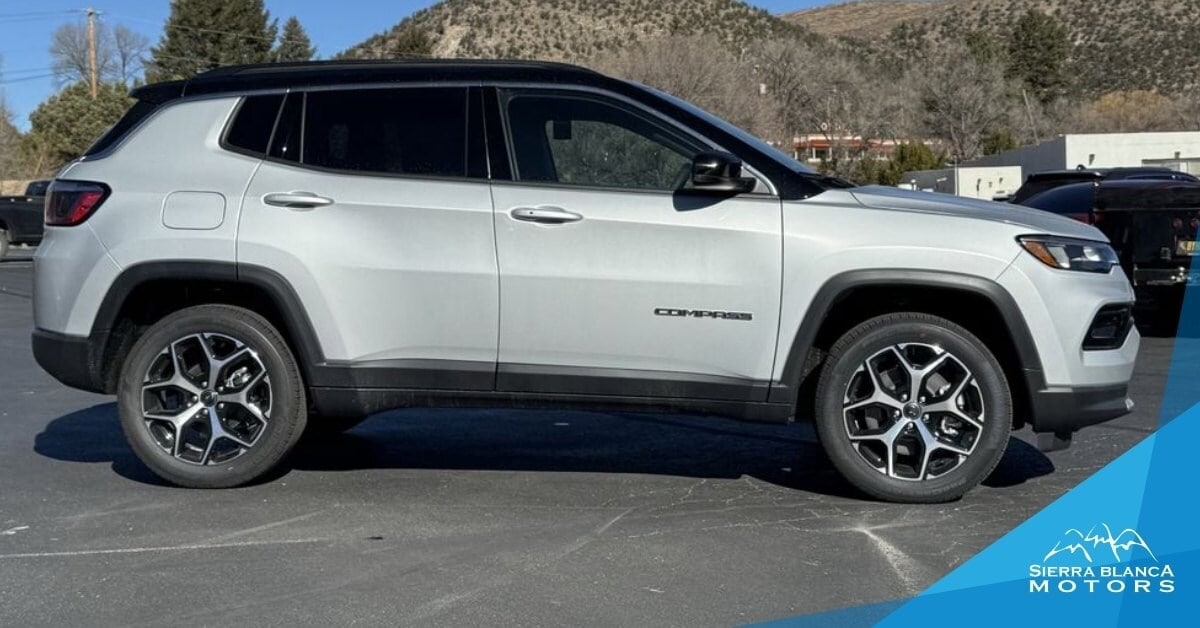 A light silver 2026 Jeep Compass SUV with a black roof and multi-spoke black and silver wheels, parked on an asphalt surface. The vehicle's 