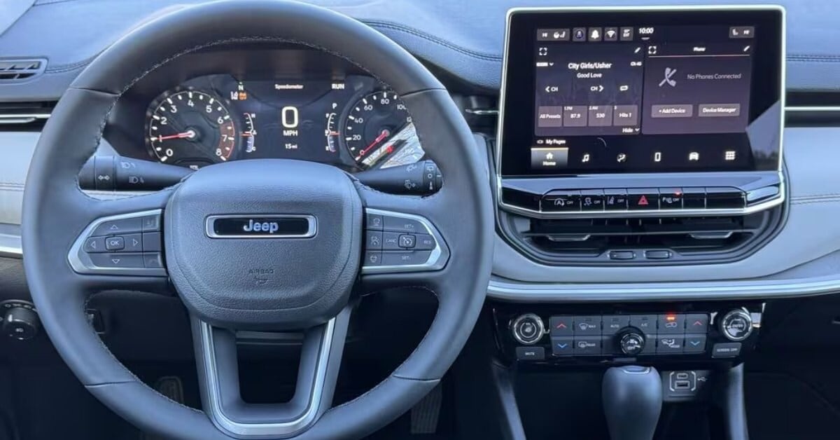 A modern 2026 Jeep Compass interior showcasing a black leather-wrapped steering wheel with the Jeep logo and multifunctional controls. Behind the wheel, a digital instrument cluster displays 