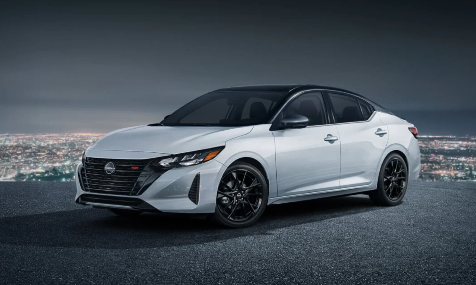 Exterior image of a white 2025 Nissan Sentra SR Midnight Edition parked on a hill at night with cityscape background views