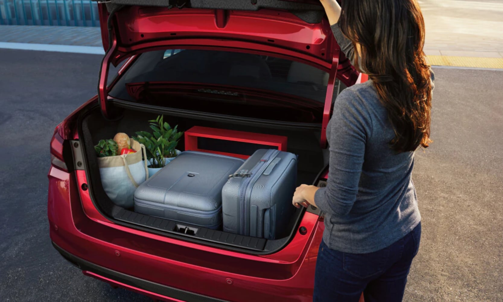 Exterior rear-view image of a person opening the 2025 Nissan Versa trunk with suitcases and groceries stored inside