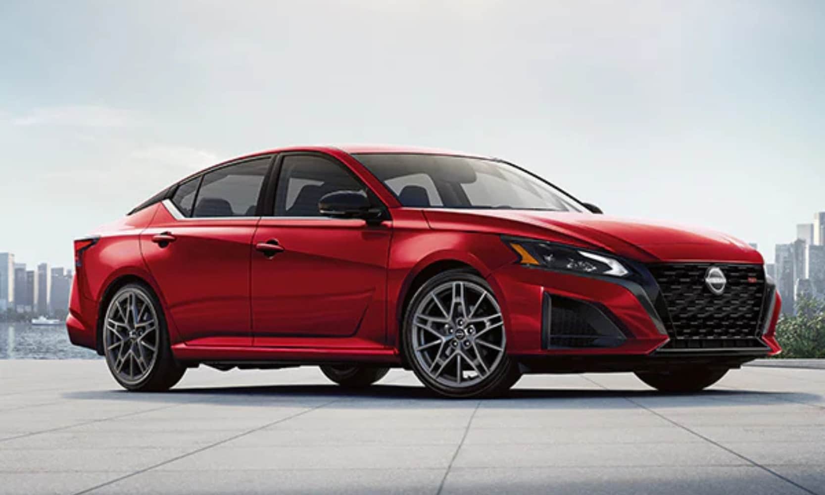 Exterior side angle image of a red 2024 Nissan Altima parked in a cityscape landscape