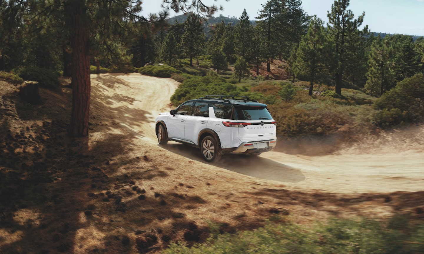 Exterior rear-view image of a white 2025 Nissan Pathfinder driving up a mountain