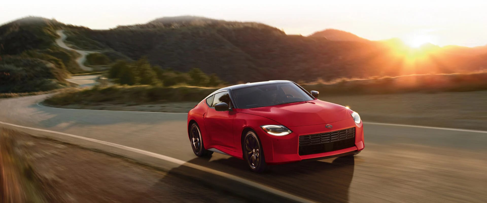 Hero front view image of a red 2025 Nissan Z driving down an open freeway with mountains in the background during sunset