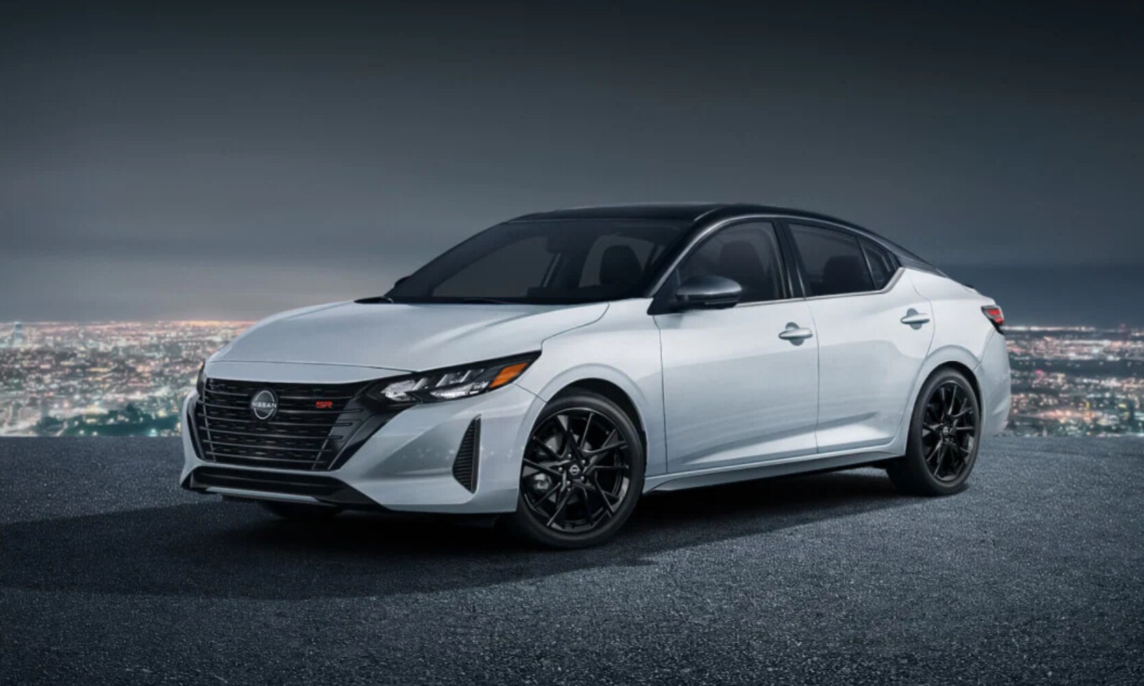 Exterior image of a white 2025 Nissan Sentra SR Midnight Edition parked on a hill at night with cityscape background views