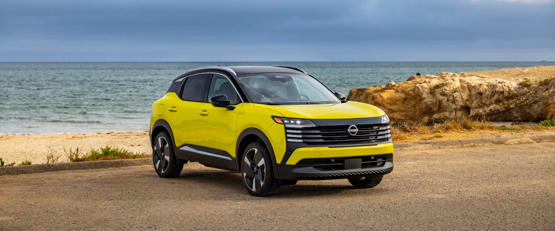Exterior image of a fluorescent yellow 2025 Nissan Kicks parked on a beach