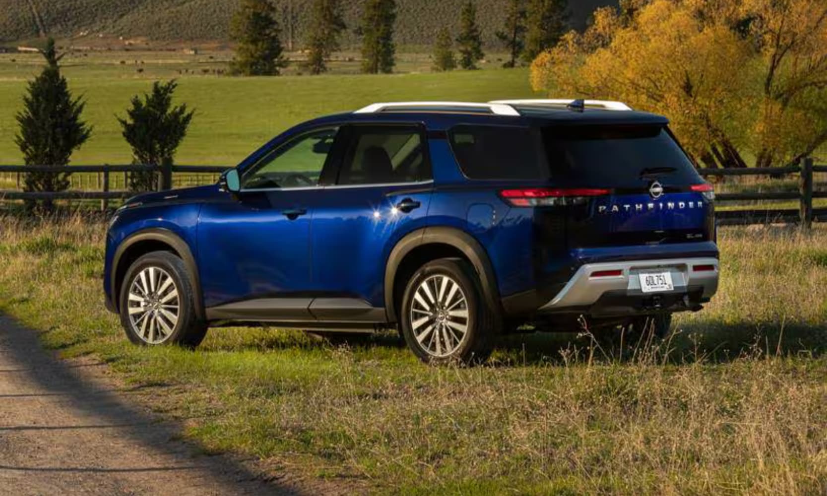 Exterior rear-view angle image of a blue 2023 Nissan Pathfinder SL parked in a grassy field