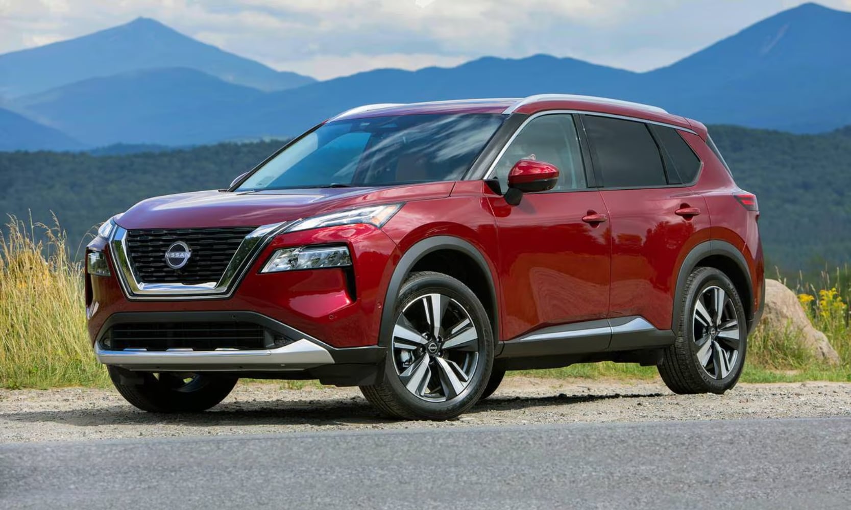 Exterior side angle image of a red 2023 Nissan Rogue parked in a natural setting with mountains behind it