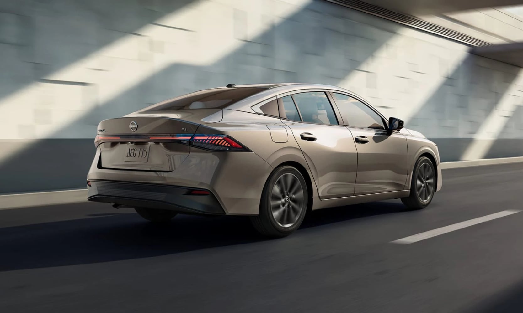 Exterior rear angle image of a light brown metallic 2026 Nissan Sentra SL driving on an enclosed freeway