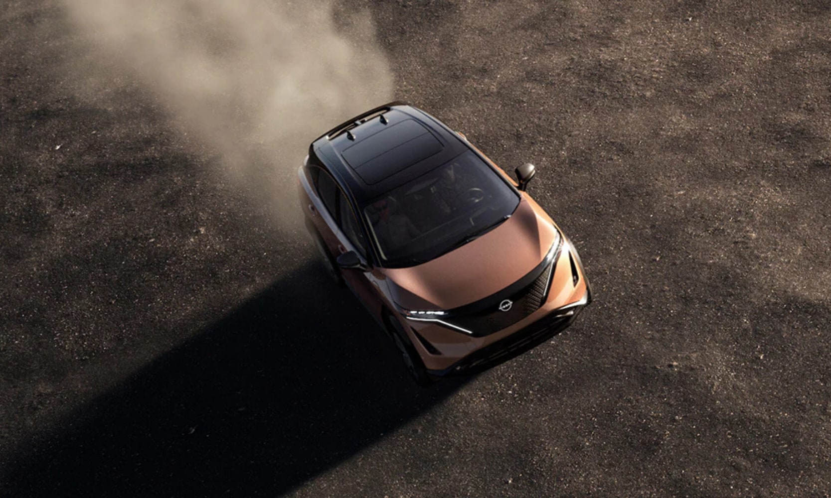 Top-view image of a copper 2025 Nissan ARIYA driving on a dirt landscape with dust blowing behind the rear wheels