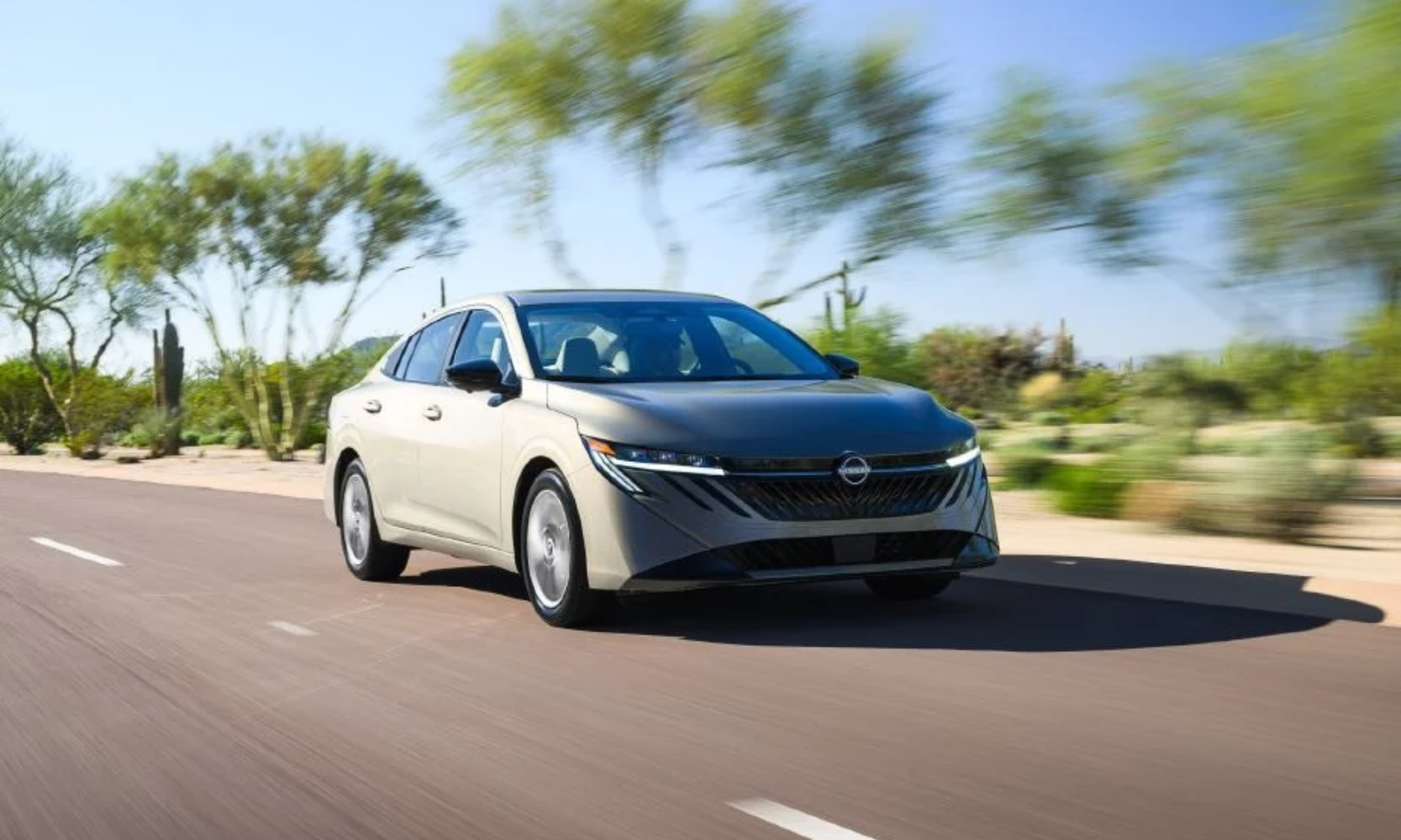 Exterior front-view image of an off-white 2027 Nissan Sentra SL driving on a tree-lined road