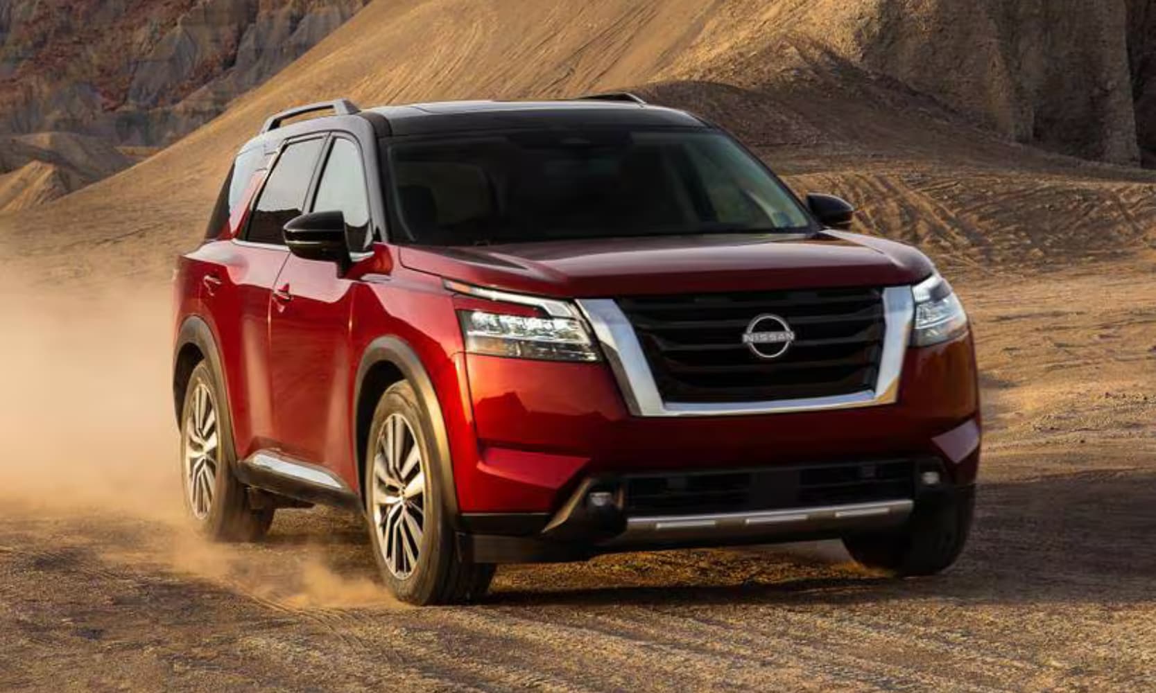 Exterior front angle image of a red 2023 Nissan Pathfinder Platinum driving through a dirt hill landscape