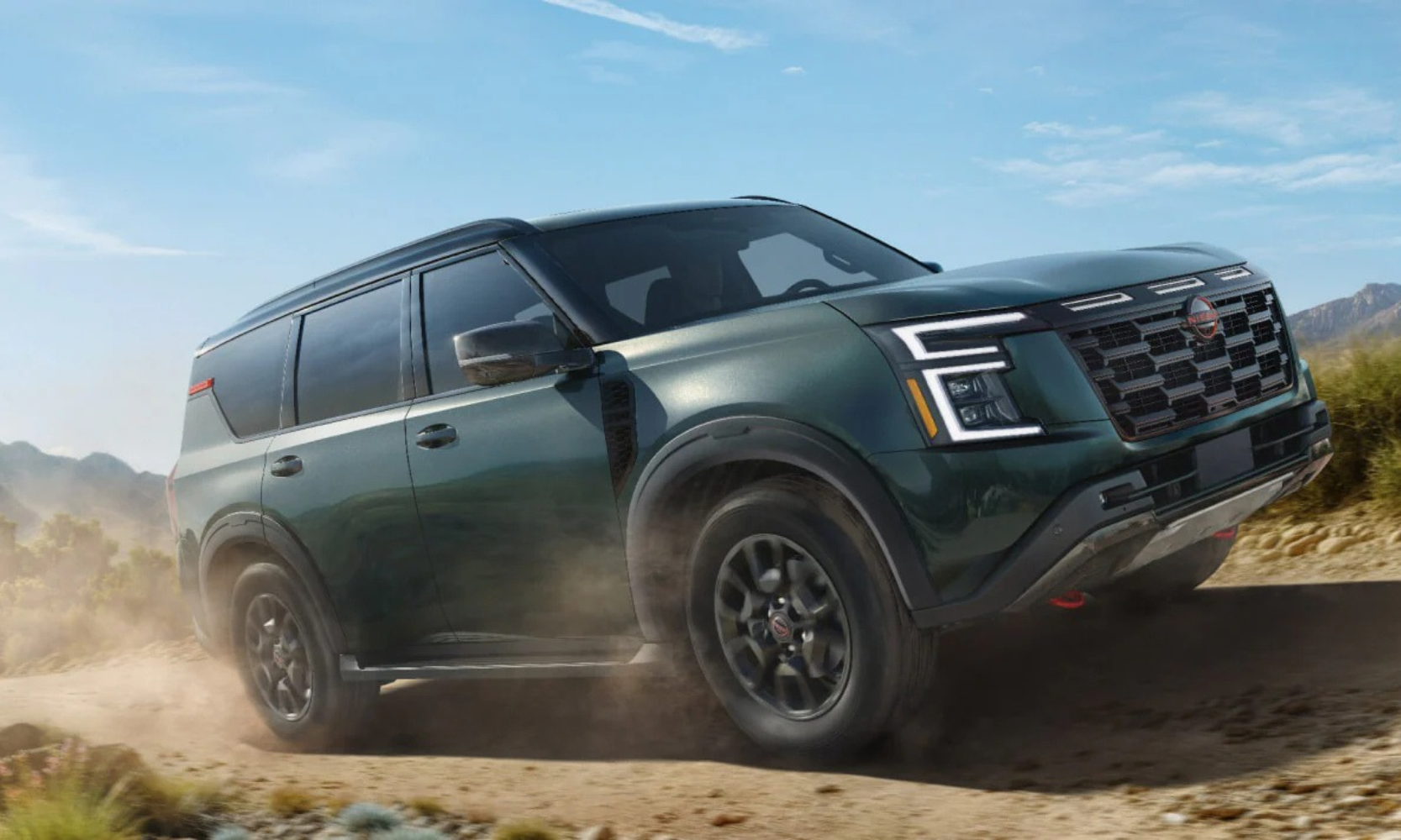 Exterior image of a green 2027 Nissan Armada driving on a dirt road with dirt blowing behind the tires