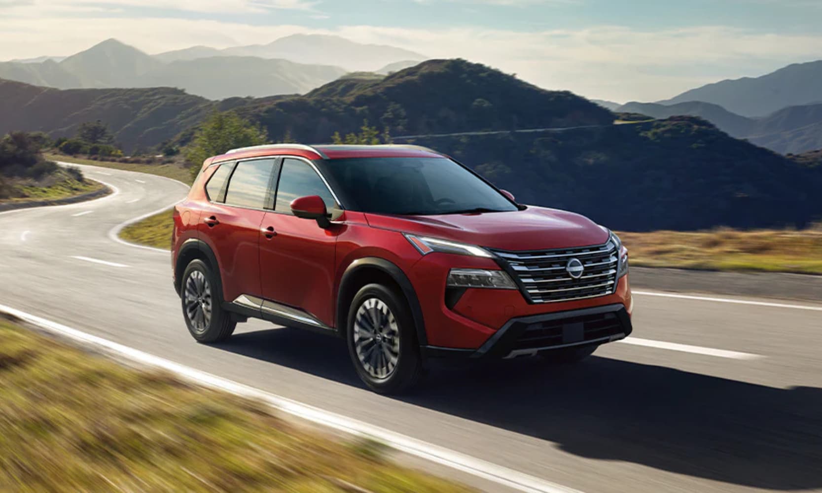Exterior image of a red 2025 Nissan Rogue Platinum driving down an open freeway with mountains in the background