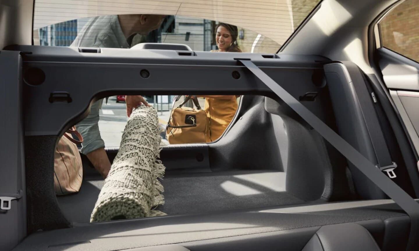 Closeup interior image of people loading a rug in an open 2025 Nissan Sentra trunk
