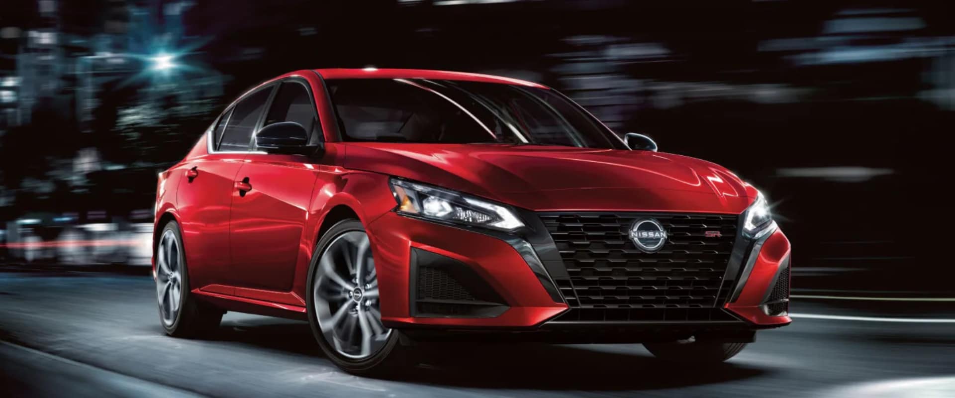 Exterior hero image of a red 2026 Nissan Altima driving on a city street at night